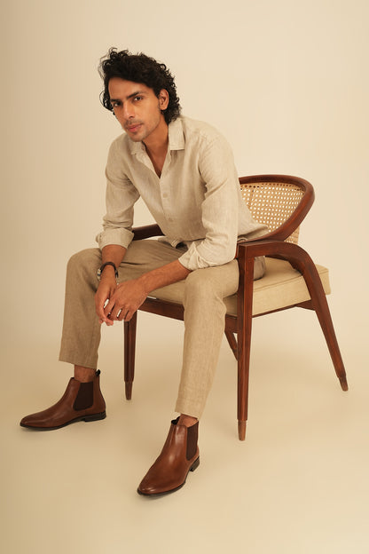 Stylish man wearing a 100% linen shirt and pure linen trousers sitting on a chair. The outfit embodies effortless luxury and a laid back lifestyle.